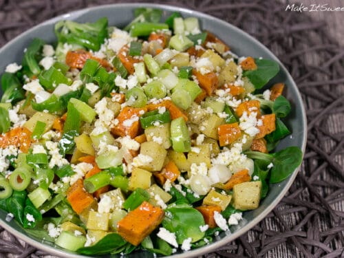 Schüssel mit Ofenkartoffel-Salat mit gehackten Süßkartoffeln, Frühlingszwiebeln, Feldsalat und zerbröckeltem Feta-Käse.