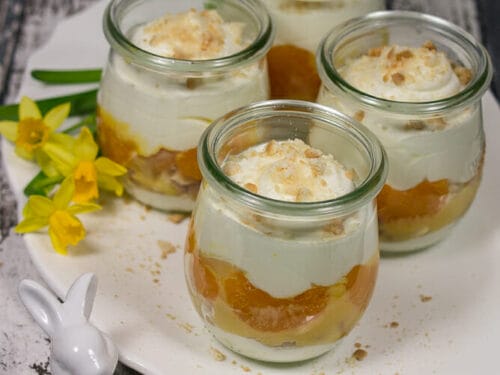 Vier Gläser Eierlikör-Tiramisu mit Streuseln, dicht nebeneinander auf einem weißen Teller angeordnet.