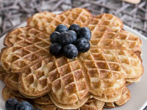 Herzförmige, zuckerfreie Waffeln auf einem weißen Teller, garniert mit frischen Blaubeeren.