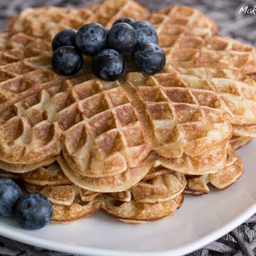Zimt Waffeln ohne Zucker 3 Ein Stapel herzförmiger zuckerfreier Waffeln mit frischen Blaubeeren auf einem weißen Teller.
