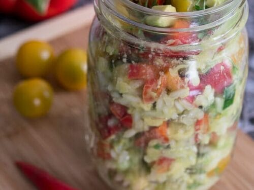 Glas Reissalat mit Avocado, Paprika, Tomaten und Chili auf einem Holzbrett.