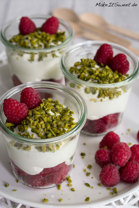 Himbeere-Pistazien-Dessert im Glas geschichtet. Unten sind Himbeeren, darauf eine Creme, mit Pistazien bestreut