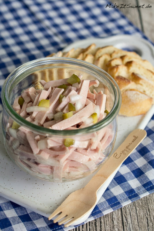 Wurstsalat ohne Käse im Glas mit Gurken und Zwiebeln. Daneben liegt Baguette