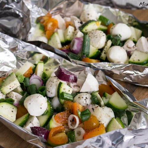 Zucchini, Tomate, Champignons und Mozzarellakugeln in Folienverpackungen, gewürzt und bereit zum Backen oder Grillen.