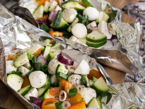 Zucchini, Tomate, Champignons und Mozzarellakugeln in Folienverpackungen auf einem Holzbrett gewürzt.