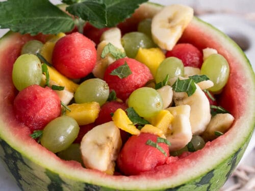 Wassermelonen Obstsalat Schale mit Weintrauben, Bananenscheiben, Melonenkugeln und Minzblättern.