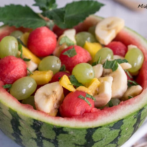 Wassermelonen Obstsalat Schale mit Weintrauben, Bananenscheiben, Melonenkugeln und Minzblättern.