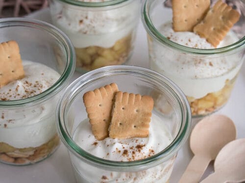 Vier Gläser Käsekuchen mit Apfel-, Sahne- und Biskuitschichten.