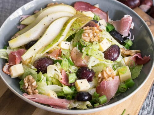 Frischer Herbstsalat mit Salat, Weintrauben, Birnenspalten, Käsewürfeln, Walnüssen, Schinken und Frühlingszwiebeln in einer Schüssel.