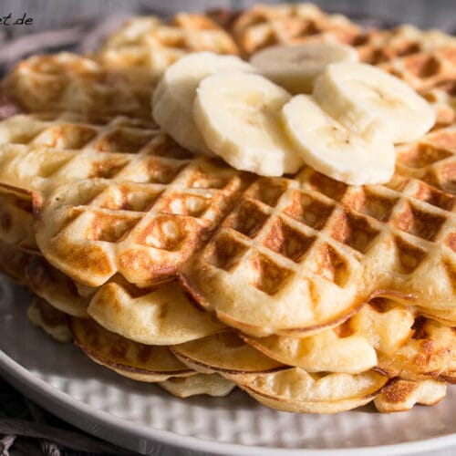 Waffeln mit Buttermilch 3 Ein Stapel Buttermilchwaffeln, belegt mit Bananenscheiben auf einem weißen Teller.