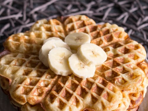 Waffeln mit Buttermilch gestapelt und mit Bananenscheiben belegt auf einem weißen Teller.