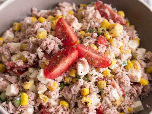 Schale mit Thunfischsalat mit Mais, Tomaten und Feta auf einer weißen Unterlage.