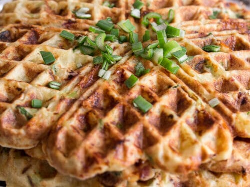 Ein Stapel herzhafter Kartoffelwaffeln mit Speck auf einem weißen Teller.