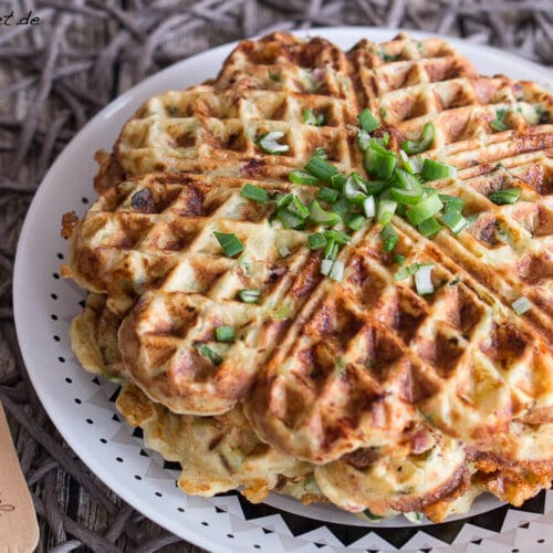 Herzhafte Kartoffelwaffeln mit Speck, die mit Frühlingszwiebeln auf einem Teller angerichtet sind.