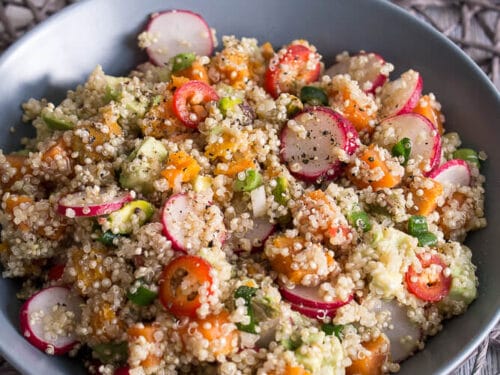 Schüssel mit Quinoa-Salat mit Avocadoscheiben, Radieschen, Süßkartoffeln und Lauchzwiebeln.