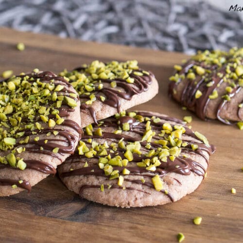 Mit Schokolade bestreute Cookies, die mit gehackten Pistazien belegt sind.