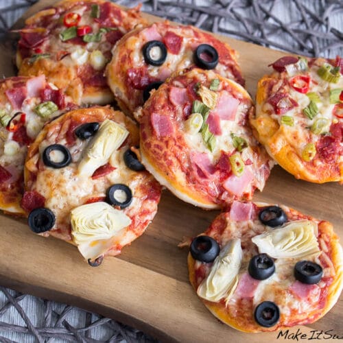 Selbstgemachte Mini-Pizzen, belegt mit Schinken, Oliven, Artischocken und Salami, angerichtet auf einem Holzbrett.