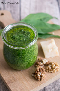 Bärlauchpesto mit Walnuss 1 Ein Glas Bärlauchpesto mit Walnüssen, Parmesan und frischen grünen Blättern auf einem Holzbrett.