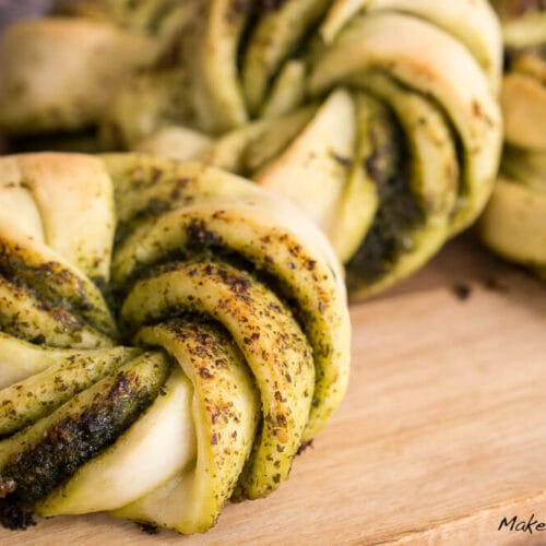 Gedrehte Pesto-Hefeknoten-Brötchen mit grünem Pesto-Strudel, aus der Nähe auf einem Holzbrett dargestellt.