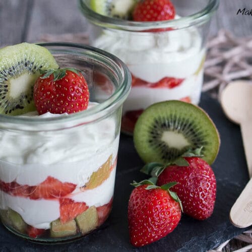 Geschichtetes Erdbeerdessert mit Kiwi und Joghurt in zwei Gläsern, gekrönt mit frischem Obst.
