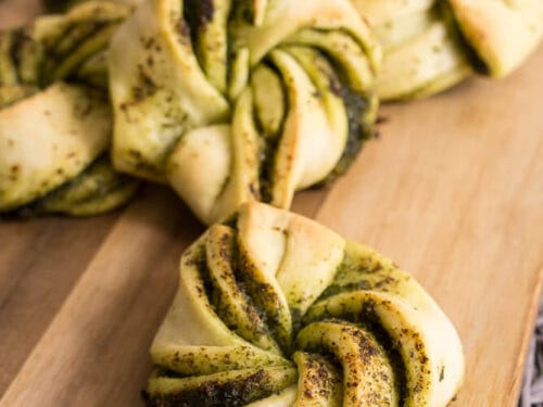 Pesto-Hefeknoten, ein mit leuchtend grünem Pesto gefülltes Strudelteiggebäck, das auf einem Holzbrett angerichtet ist.