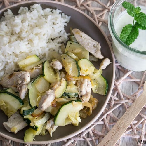 Weißer Reis mit Hühnerfleisch und Zucchini, serviert auf einem Teller mit einem Joghurt aus dem Glas und Minze.