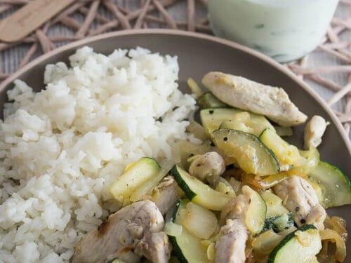 Teller mit weißem Reis und Hähnchen sowie Zucchini, serviert mit einem Glas Joghurt mit Minze.