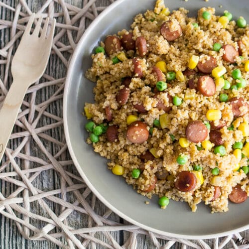 Couscous mit geschnittener Wurst, Erbsen und Mais auf einem Teller.