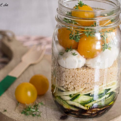 Couscous Salat mit Mozzarella und Zucchini - Salat im Glas 3 Schichtsalat aus gelben Tomaten, Mozzarella, Couscous und Zucchini in einem Einmachglas auf einem Holzbrett.