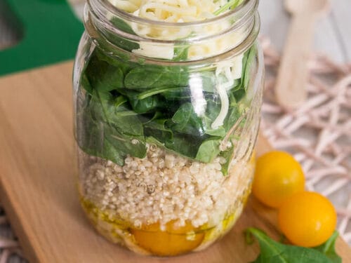 Salat im Glas mit Quinoa, Spinat, gelben Tomaten und geriebenem Käse auf einem Holzbrett geschichtet.