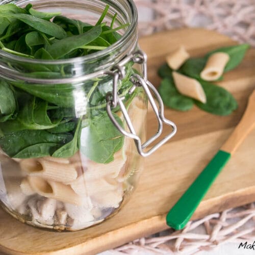 Schichtsalat gefüllt mit Spinat, Vollkornnudel und Hähnchen auf einem Holzbrett mit losen Nudeln und einer Gabel.