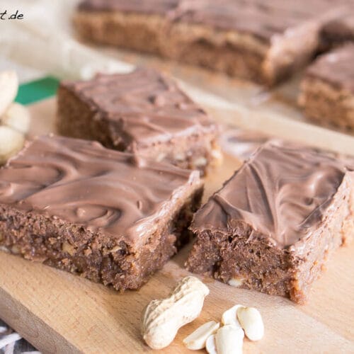 Erdnuss Brownies mit Noisette 3 Schokoladenüberzogene Brownies mit ganzen Erdnussstücken auf einem Holzbrett.