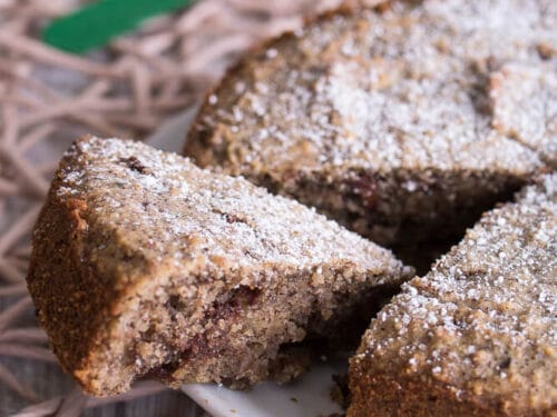 In Scheiben geschnittener Nusskuchen ohne Mehl, mit Puderzucker bestäubt, auf einem weißen Teller.