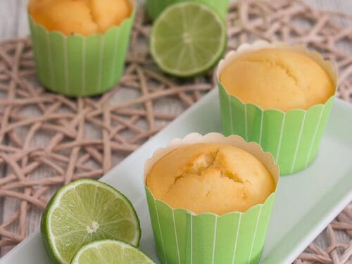Vier Limettenmuffins in grüner Verpackung auf einem Teller mit geschnittenen Limetten.