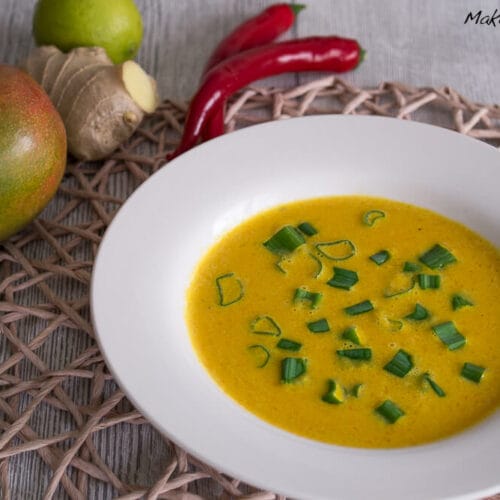 Scharfe Mango-Karotten-Suppe mit Kokos 3 Schale mit Mango-Karotten-Suppe, die mit Frühlingszwiebeln, Mango, Kokosmilch und Chili garniert ist.