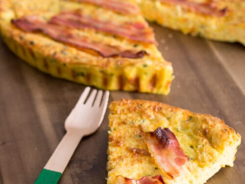 Eine Scheibe Tarte mit Bacon auf einem Holzbrett.
