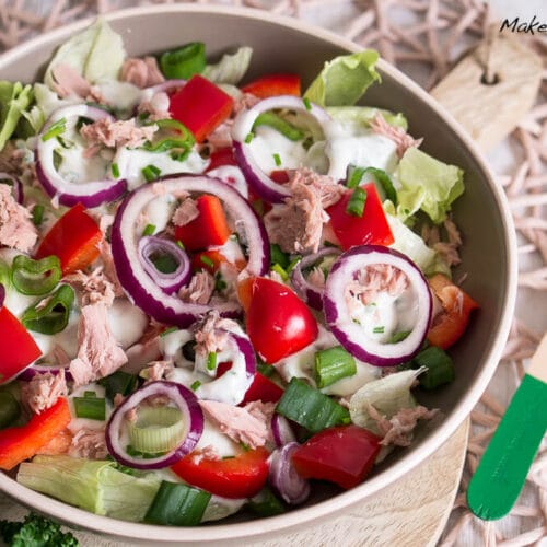 Thunfischsalat mit Kopfsalat, roten Zwiebeln, Paprika und grünen Zwiebeln in einer Schüssel, übergossen mit Joghurt-Dressing.