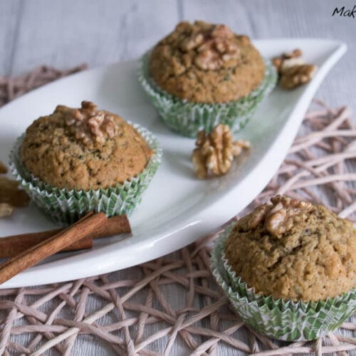 Zucchini Muffins mit Walnuss 3 Drei Zucchini-Walnuss-Muffins in grünen Verpackungen auf einem weißen Teller.