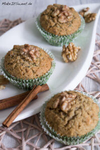 Drei Zucchini-Muffins, belegt mit Walnüssen, auf einem weißen Teller.