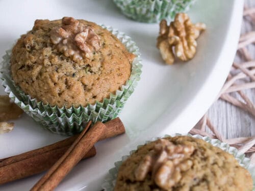 Drei Zucchini-Muffins, belegt mit Walnüssen, auf einem weißen Teller.