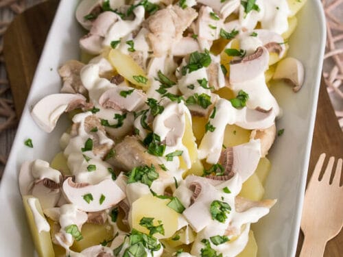 Ein weißer Teller mit Kartoffelsalat mit Champignons und einem Schmand-Dressing.