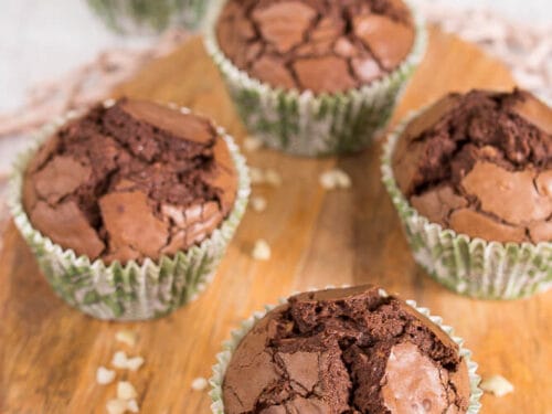 Fünf glutenfreie Schokoladenmuffins mit Nutella in grünen Papierförmchen auf einem Holzbrett.
