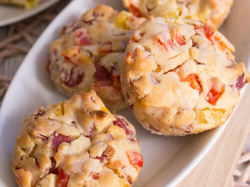 Vier herzhafte Muffins mit Salami und roten Paprikastücken auf einem weißen Teller.