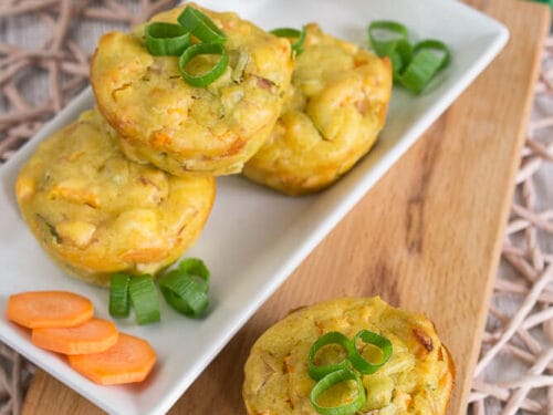 Fünf Putenmuffins mit Karotten, Curry und Frühlingszwiebeln auf einem Teller und einem Brett.