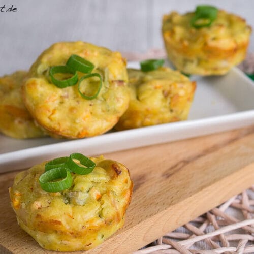 Vier herzhafte Muffins mit Pute, Karotten und Curry serviert auf einem Holzbrett und einem Teller.