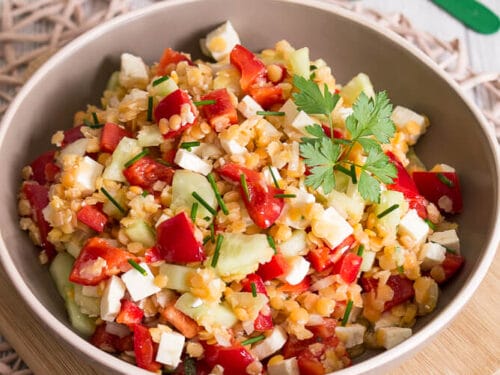 Schüssel mit Linsensalat mit Paprika, Gurken, Feta und Petersilie.