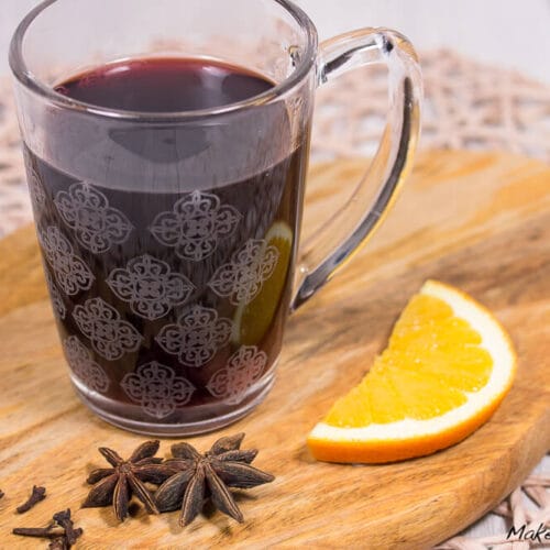 Glühwein selber machen 3 Ein Glas Glühwein mit einer Orangenscheibe, Zimtstangen und Sternanis auf einem Holzbrett.