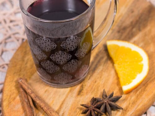 Glasbecher mit Glühwein, garniert mit Orangenscheibe, Zimtstangen, Sternanis und Nelken.