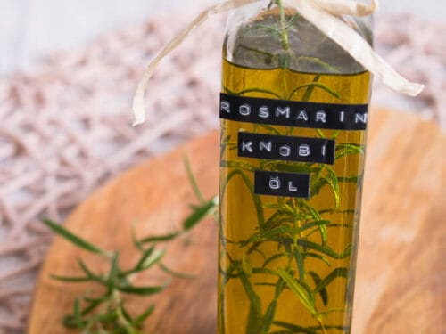 Glasflasche mit Rosmarin-Knoblauch-Öl mit Kräutern darin.