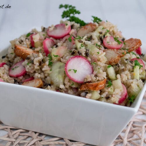 Schale mit Wildreissalat, Radieschen, Gurkenscheiben, gegrillten Hähnchenstücken und frischen Kräutern.